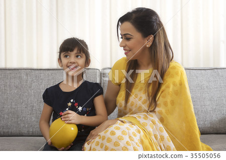 Mother and daughter sitting together with clay piggybank 35505056