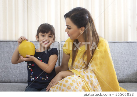 Mother and daughter sitting together holding clay piggybank 35505058