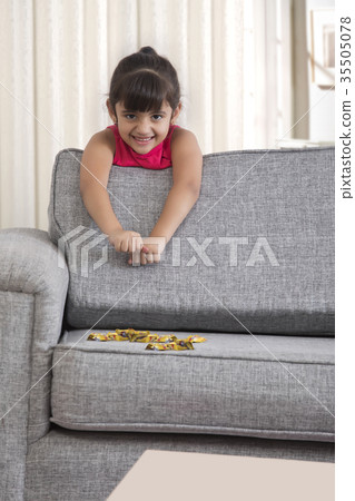 Little girl leaning on sofa with chocolate candy Little girl leaning on sofa with chocolate candy 35505078