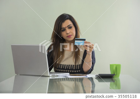 Woman shopping online from mobile phone and credit card sitting at table with laptop Woman shopping online from mobile phone and credit card sitting at table with laptop 35505118