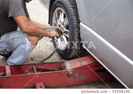 Mechanic changing car wheel with ipneumatic wrench 35509140