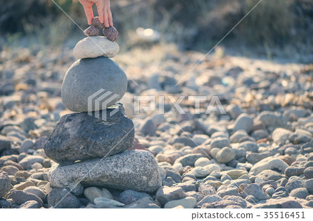 A female hand puts a small stone on pyramid A female hand puts a small stone on pyramid 35516451