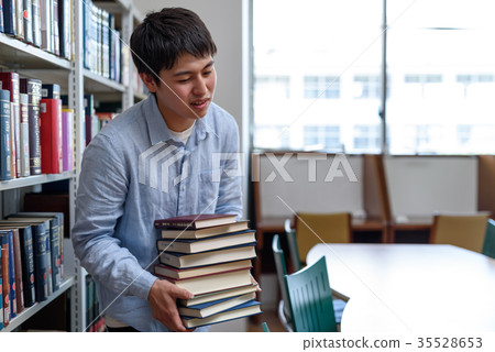Student holding pile of books in library Student holding pile of books in library 35528653