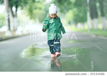 cheerful little girl walks and jumps in puddles in the rain 35533480