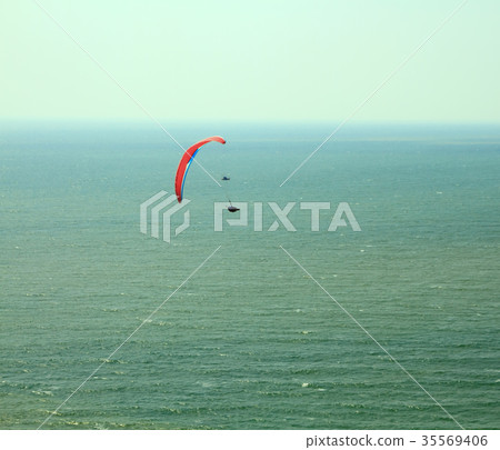 Red paraglider flying in blue sky over the ocean. 35569406