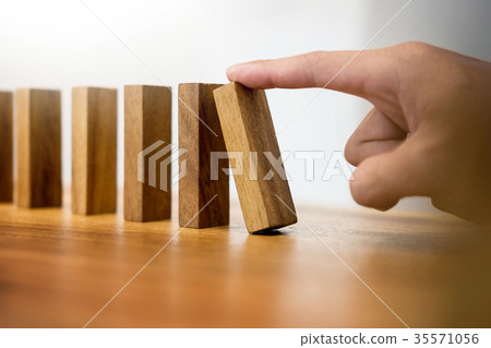 Hand of business man pushing dominoes for start on wooden backgr Hand of business man pushing dominoes for start on wooden backgr 35571056