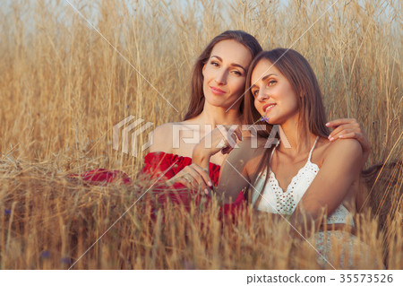 Young women are sitting in tall grass. 35573526