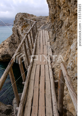 Flimsy old bridge across the rocks on sea coast 35578885