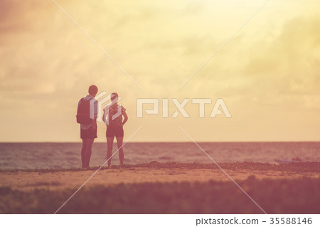 Silhouette of couple people or tourist standing on the beach in sunset time. Warm tone and vintage filter effect 35588146
