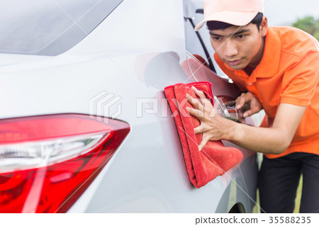 Young man using red microfiber cloth cleaning body of new silver car. For car maintenance concept.. Young man using red microfiber cloth cleaning body of new silver car. For car maintenance concept.. 35588235
