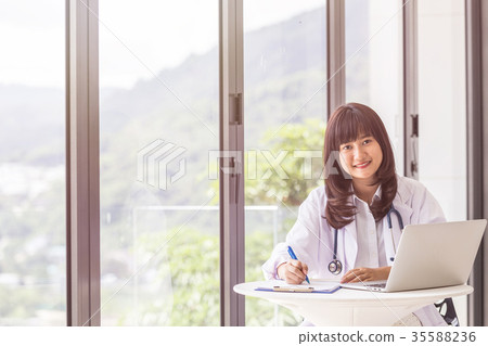 Female doctor working with her laptop beside the windows at the hospital. Looking and smiling to camera. For medical and health care concept Female doctor working with her laptop beside the windows at the hospital. Looking and smiling to camera. For medical and health care concept 35588236