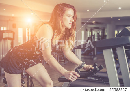 Young caucasian woman doing exercise with exercise equipment and machine in gym. Health and fitness concept. Vintage color and warm lens flare filter effect 35588237