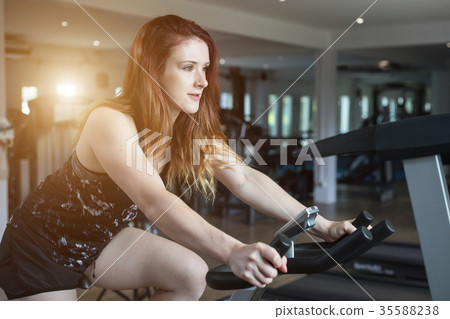 Young caucasian woman doing exercise with exercise equipment and machine in gym. Health and fitness concept. Vintage color and warm lens flare filter effect Young caucasian woman doing exercise with exercise equipment and machine in gym. Health and fitness concept. Vintage color and warm lens flare filter effect 35588238