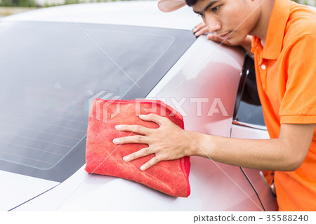 Young man using red microfiber cloth cleaning body of new silver car. For car maintenance concept.. 35588240