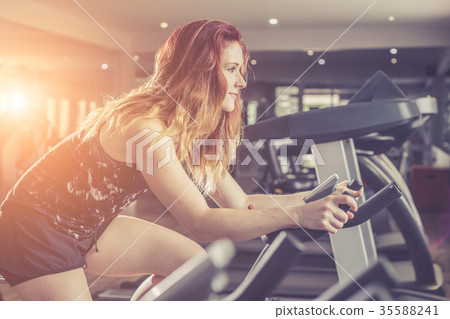Young caucasian woman doing exercise with exercise equipment and machine in gym. Health and fitness concept. Vintage color and warm lens flare filter effect 35588241