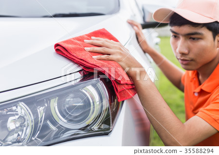 Young man using red microfiber cloth cleaning body of new silver car. For car maintenance concept.. Young man using red microfiber cloth cleaning body of new silver car. For car maintenance concept.. 35588294