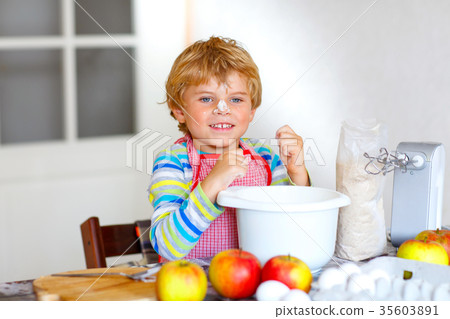 Funny blond kid boy baking apple cake indoors 35603891