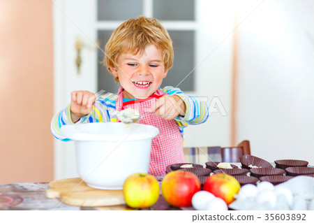 Funny blond kid boy baking apple cake indoors 35603892