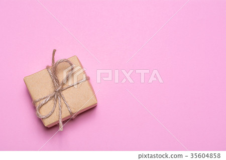A gift wrapped in kraft paper on a pink background. View from above, flat lay design. 35604858