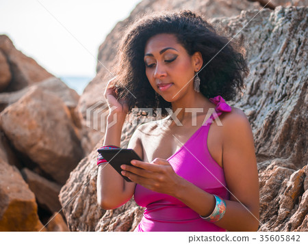 afro girl reading e-book on tropical rocks beach 35605842