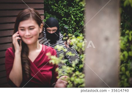 Thief is holding a gun and looking at asian woman 35614740