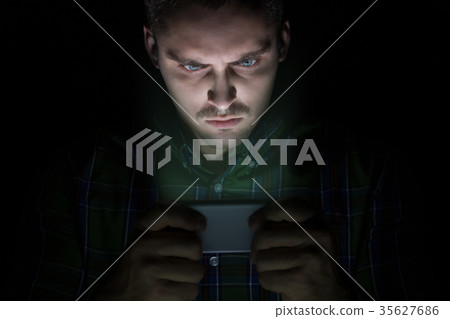 guy sits in the dark and looks at mobile phone. guy sits in the dark and looks at mobile phone. 35627686