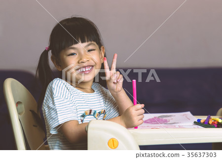 Asian girl shows two fingers or victory sign at table and hold c 35637303