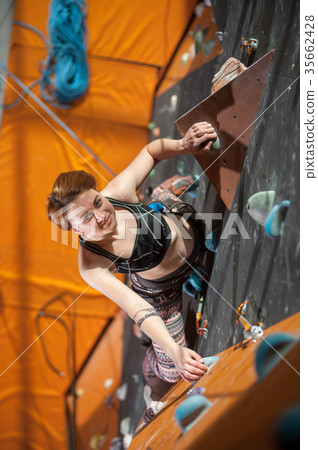 Female climber is climbing up on indoor rock-climbing wall Female climber is climbing up on indoor rock-climbing wall 35662428