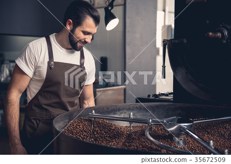 Happy unshaven worker looking at coffee beans 35672509