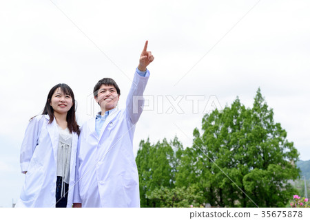Student man and woman in a white coat pointing at the sky Student man and woman in a white coat pointing at the sky 35675878