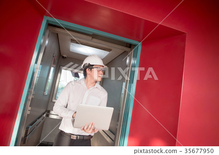 Young Asian engineer holding laptop in elevator 35677950