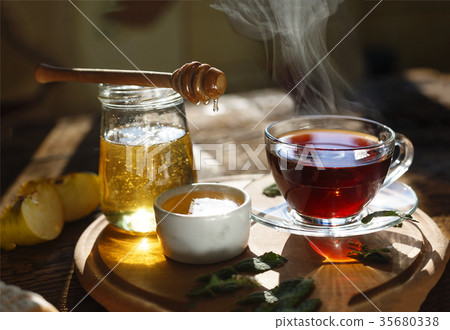 A cup of black tea, honey, mint leaves, apples. 35680338