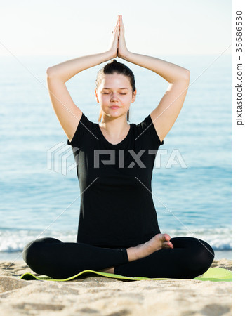Smiling adult female in black T-shirt is sitting and practicing pranayama 35686530