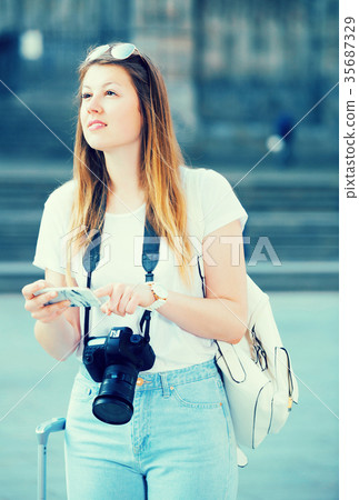 Smiling girl tourist is looking up the way in phone Smiling girl tourist is looking up the way in phone 35687329