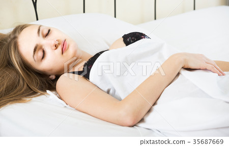 woman lying in bed under sheet with closed eyes 35687669