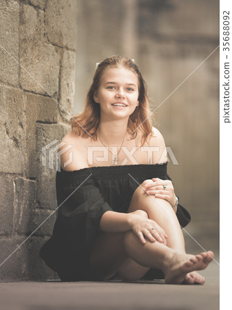 Positive girl sitting barefoot near the stone wall Positive girl sitting barefoot near the stone wall 35688092