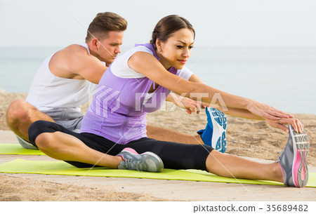 guy and girl practising yoga poses sitting on beach by sea at daytime guy and girl practising yoga poses sitting on beach by sea at daytime 35689482