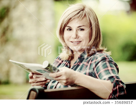 Portrait of mature woman sitting on bench and reading book in garden Portrait of mature woman sitting on bench and reading book in garden 35689857