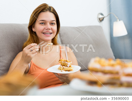 smiling female eating sweet cake on sofa smiling female eating sweet cake on sofa 35690003
