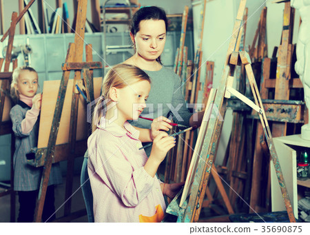 Woman teacher assisting girl during painting class 35690875
