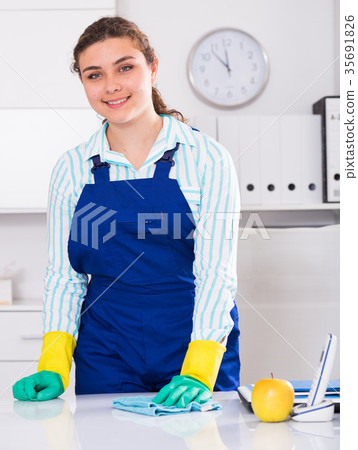 Cheerful female cleaner is cleaning dust from the desk 35691826