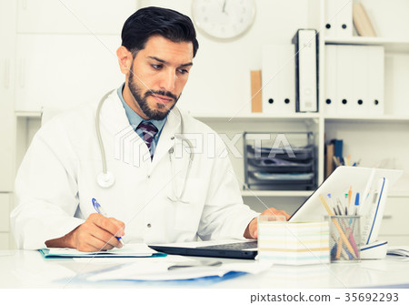 Spanish man doctor is working with documents behind laptop 35692293