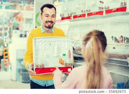 Male seller showing cage with canary bird to girl in pet shop 35692673