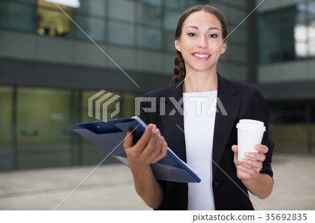 Woman office manager is examining documents and drinking coffee Woman office manager is examining documents and drinking coffee 35692835
