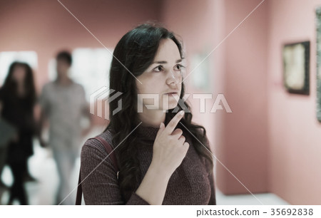 Woman attentively looking at paintings in art museum Woman attentively looking at paintings in art museum 35692838