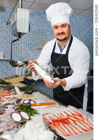 Seller in white cap and black apron showing counter with fish Seller in white cap and black apron showing counter with fish 35692840