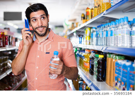 Man is choosing water with help mobile in supermarket. Man is choosing water with help mobile in supermarket. 35693184