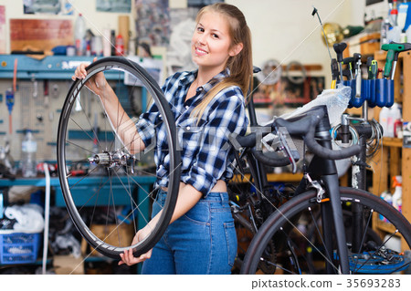 Portrait of girl who is working and replacing wheels with another one in workshop. 35693283