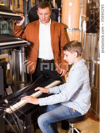 Father and teenage son examining keyboards in guitar shop 35693293