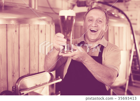 Adult brewer is standing with golden beer in glass Adult brewer is standing with golden beer in glass 35693413
